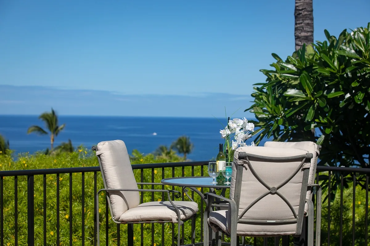 An outdoor seating area overlooks the ocean, with flowers on a small table.