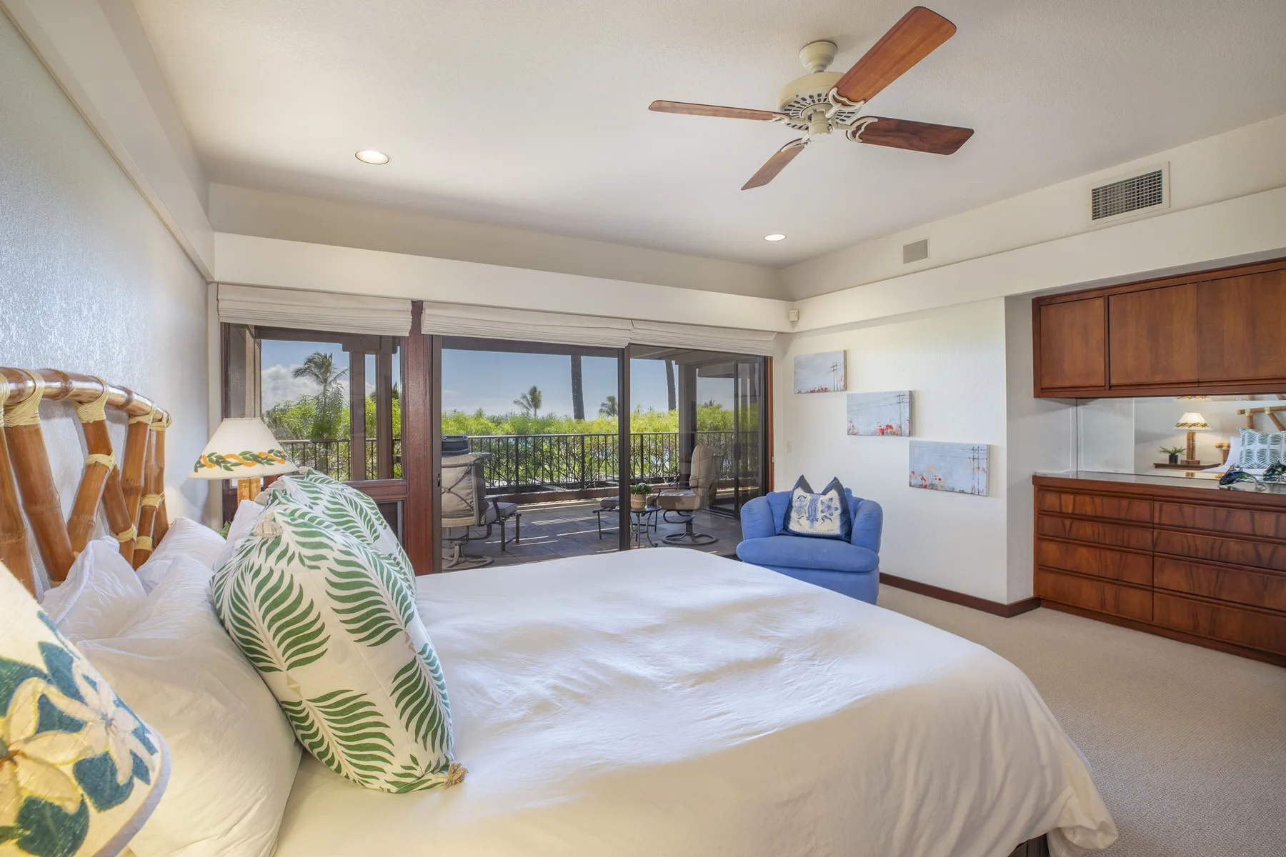 A bedroom with a large bed, a blue armchair, and sliding glass doors to a balcony.