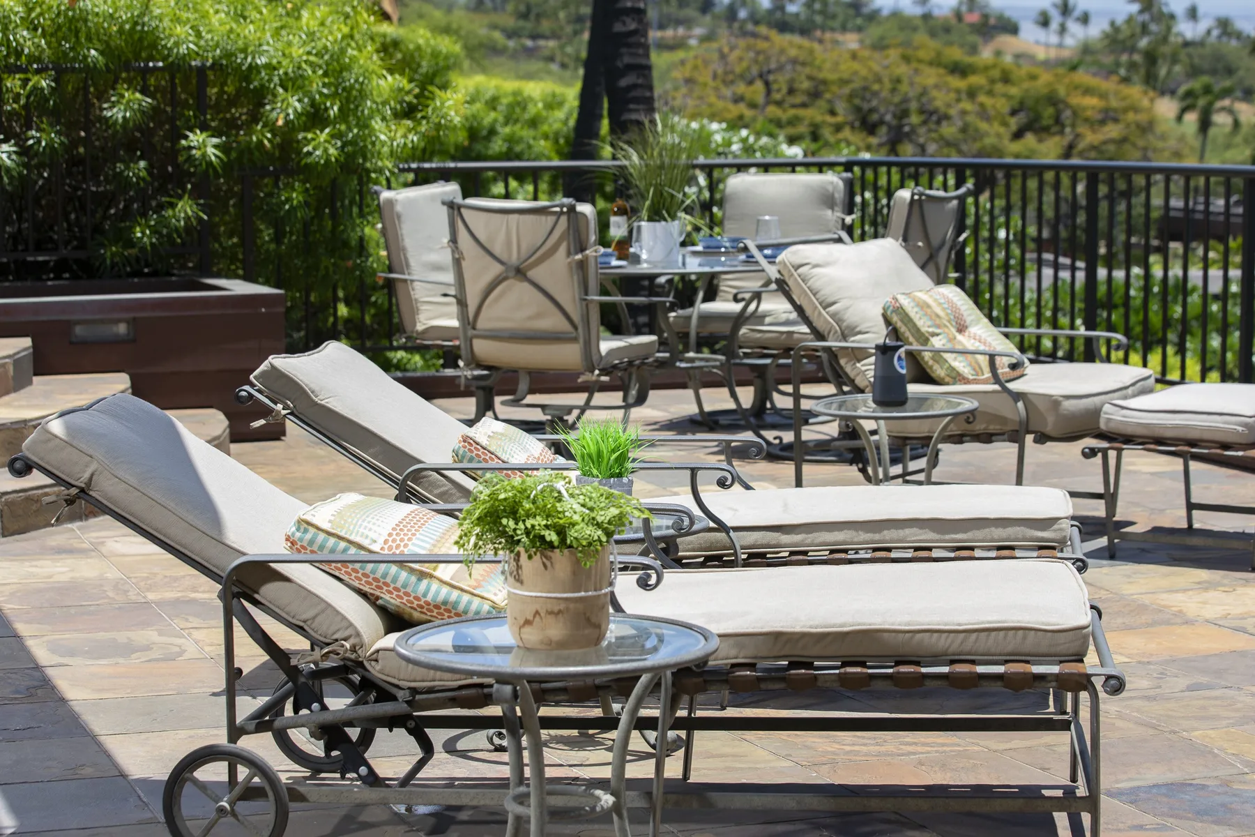 An outdoor patio has cushioned seating, small tables, and greenery along a railing.