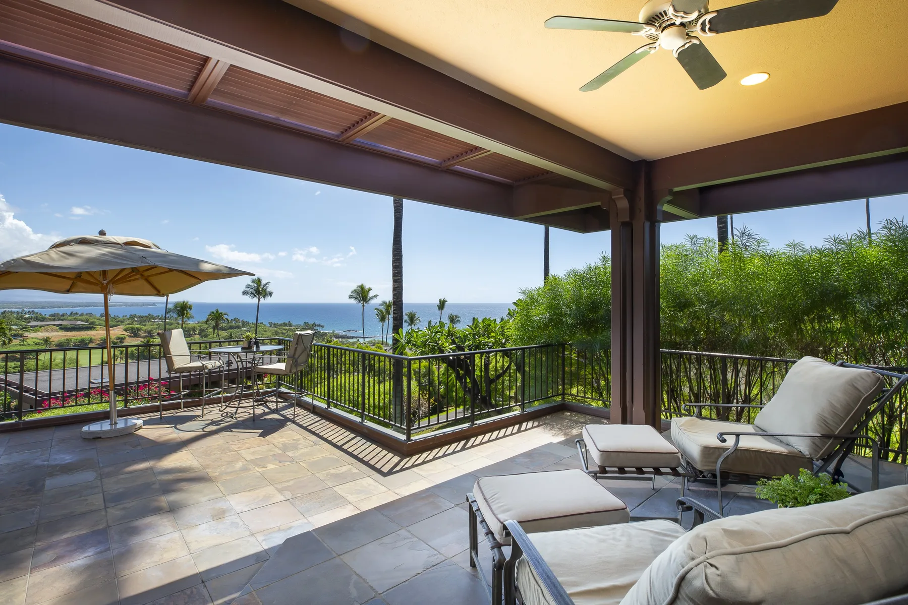 A covered outdoor patio with lounge seating overlooks a green landscape and the ocean.