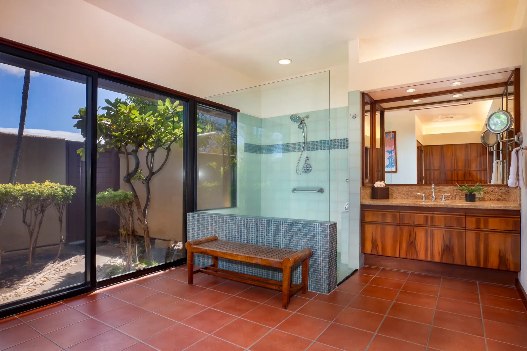 A bathroom with a glass shower area and a wooden bench beside large windows.