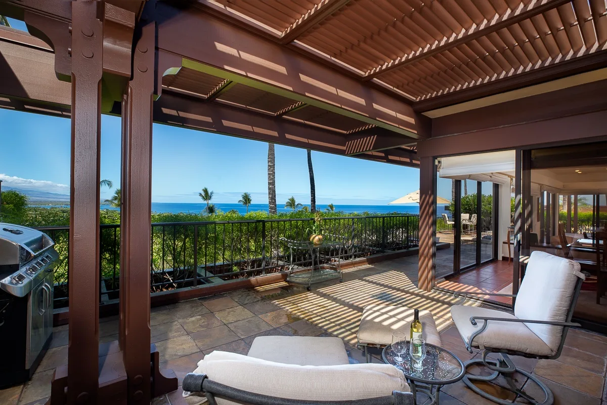 A covered patio with seating overlooks a garden and the ocean.