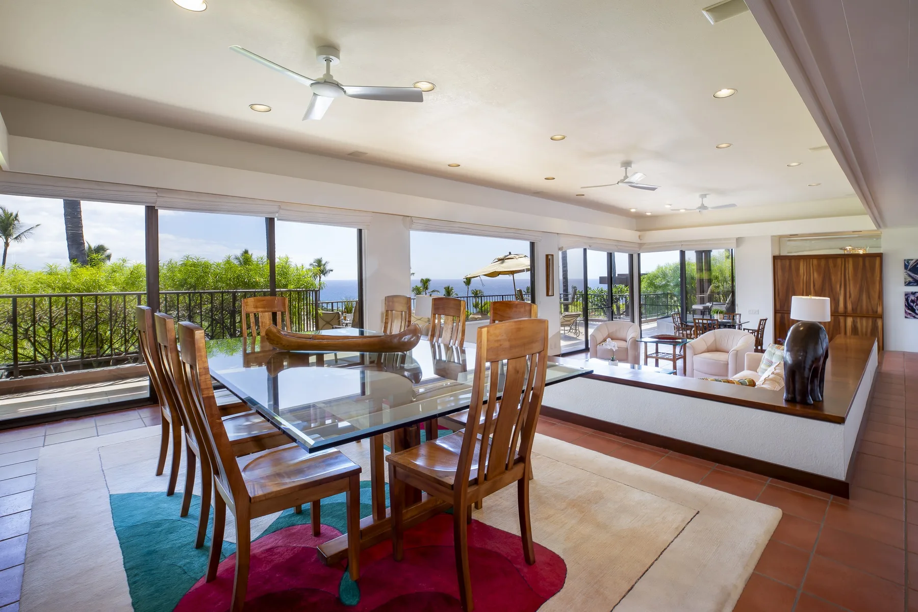 A dining area with a glass table and large windows overlooking greenery.