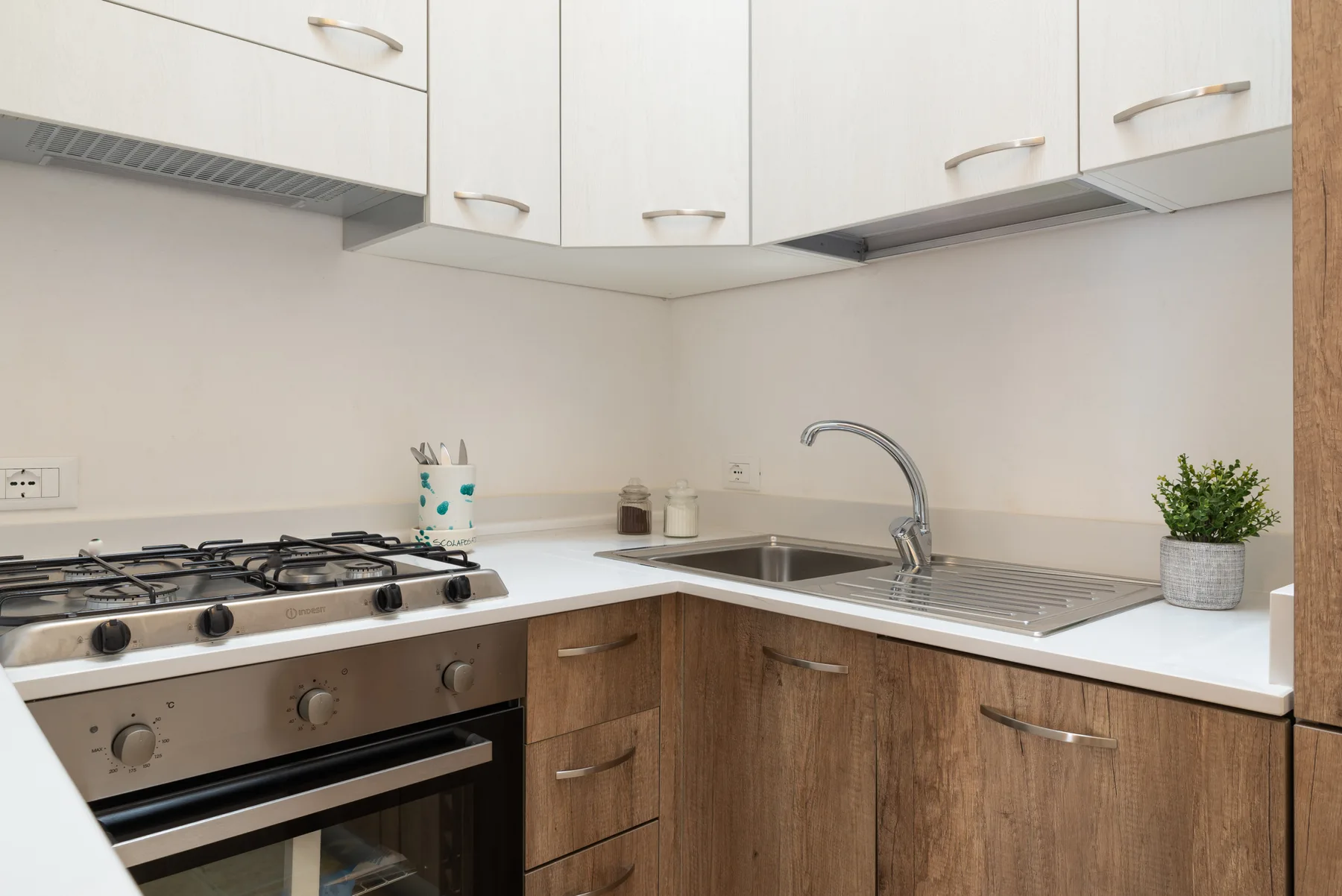 A kitchen with a gas cooktop, oven, sink, and white upper cabinets.