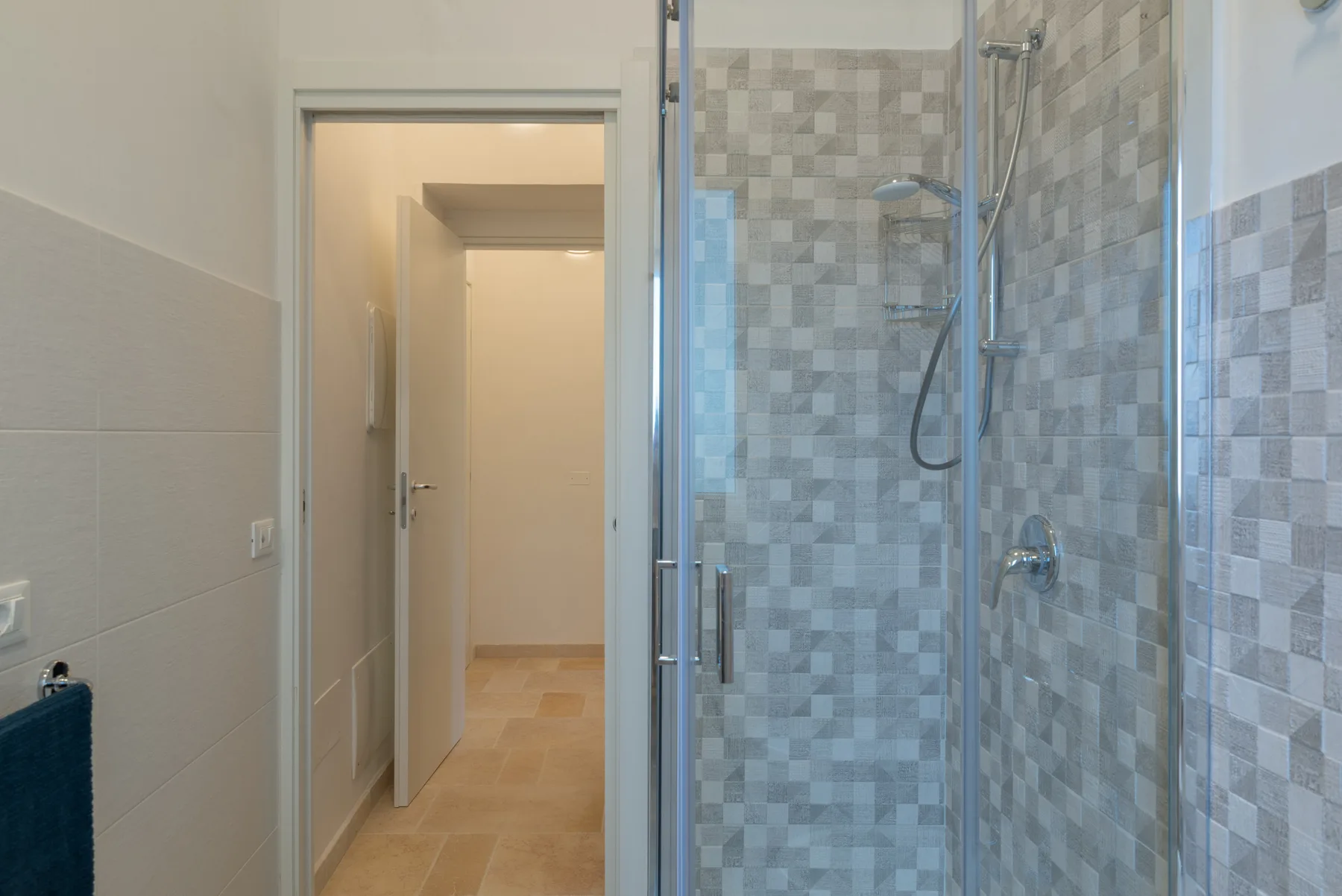 A tiled bathroom with a glass shower and an open doorway.