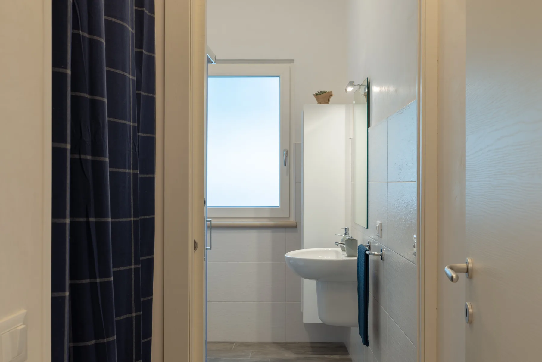 A bathroom with a shower curtain, sink, and window.