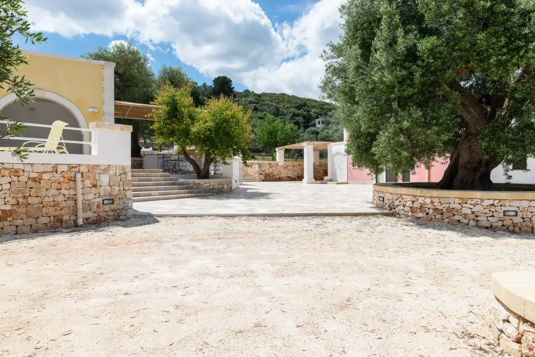 A sunny courtyard with stone walls, trees, and a paved open area.