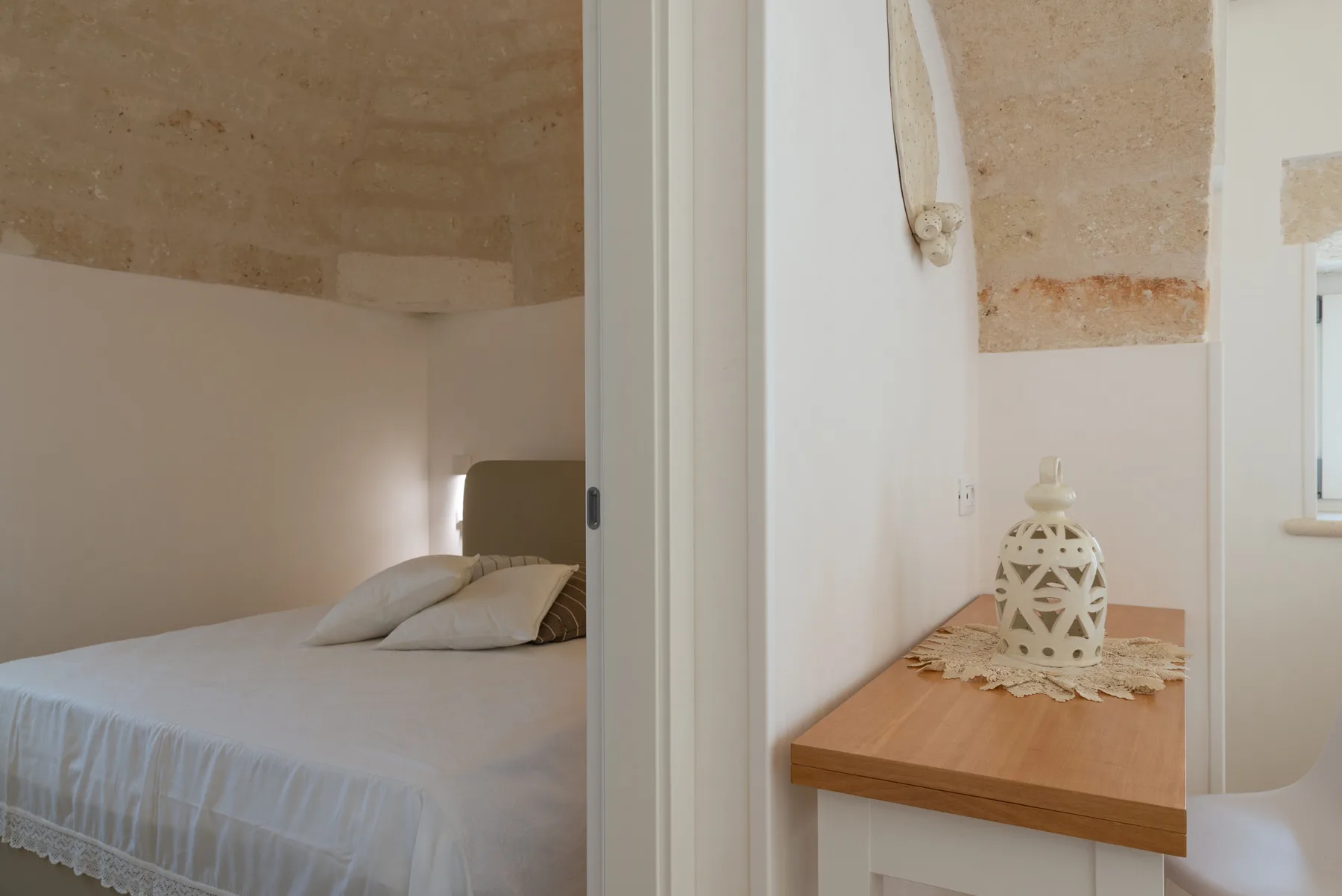 A bedroom with a bed beside a wooden console topped with a decorative vase.