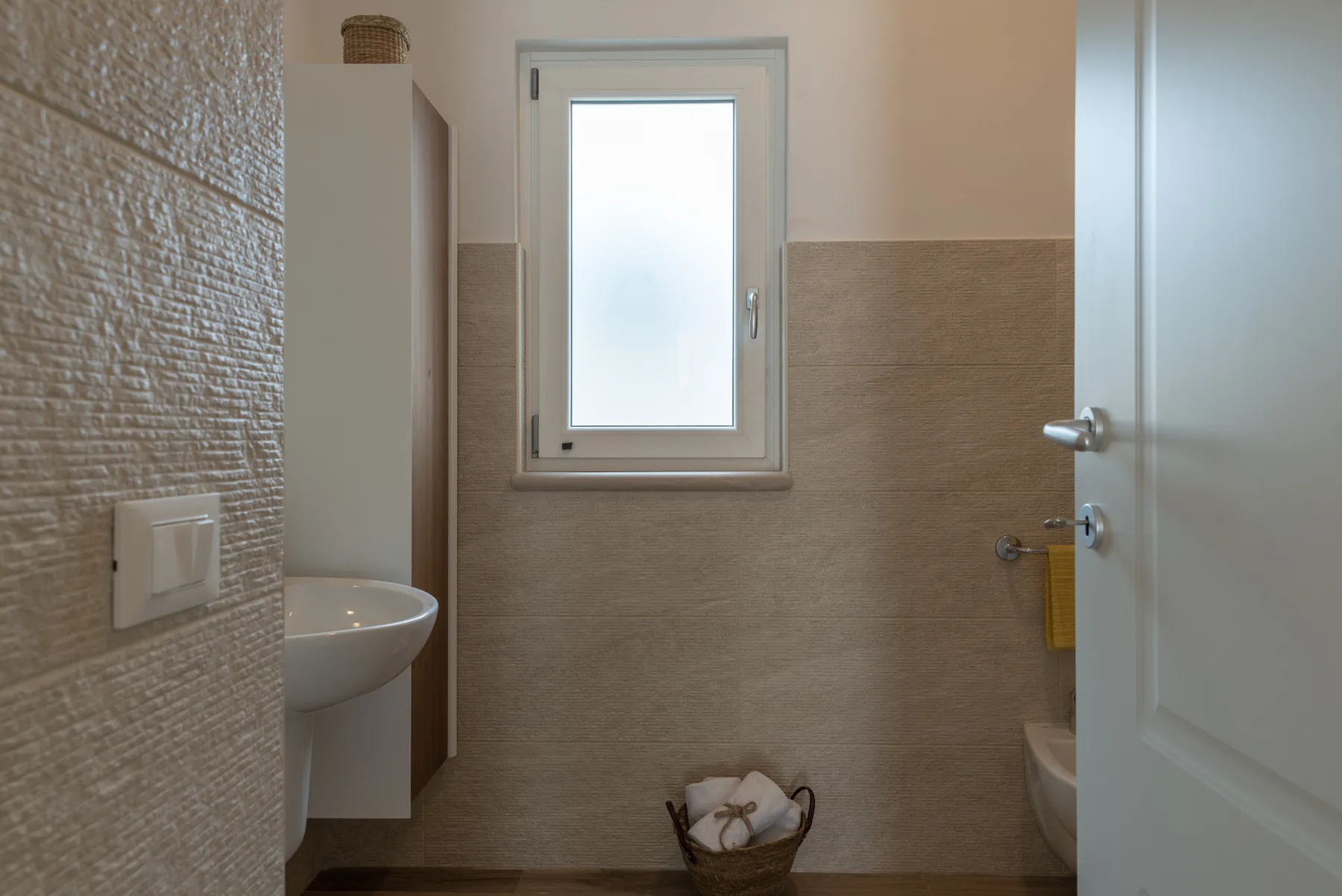 A bathroom with tiled walls, a small window, and a partially open door.