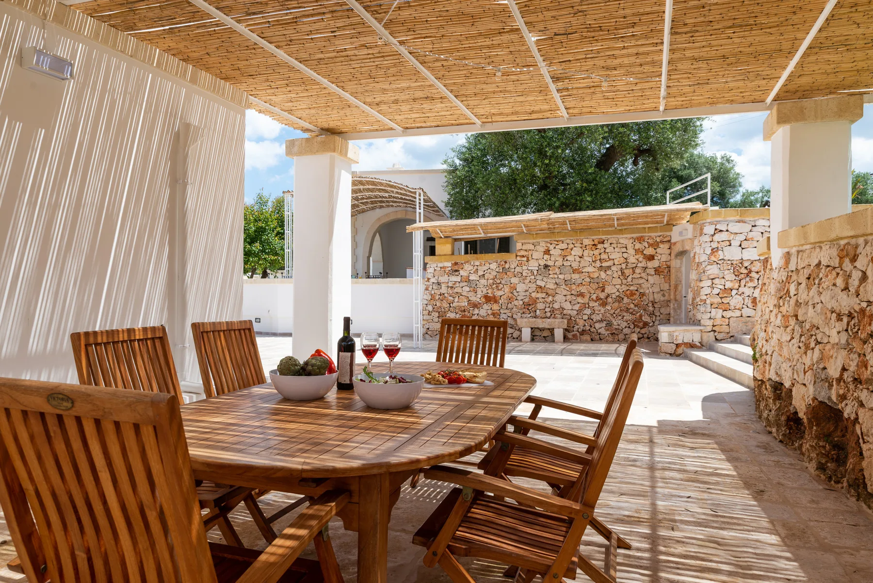 A covered outdoor dining area with a wooden table beside a stone wall.