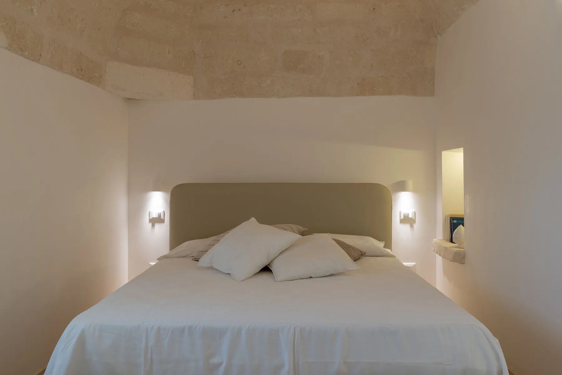 A bedroom with a neatly made bed and wall-mounted lights.
