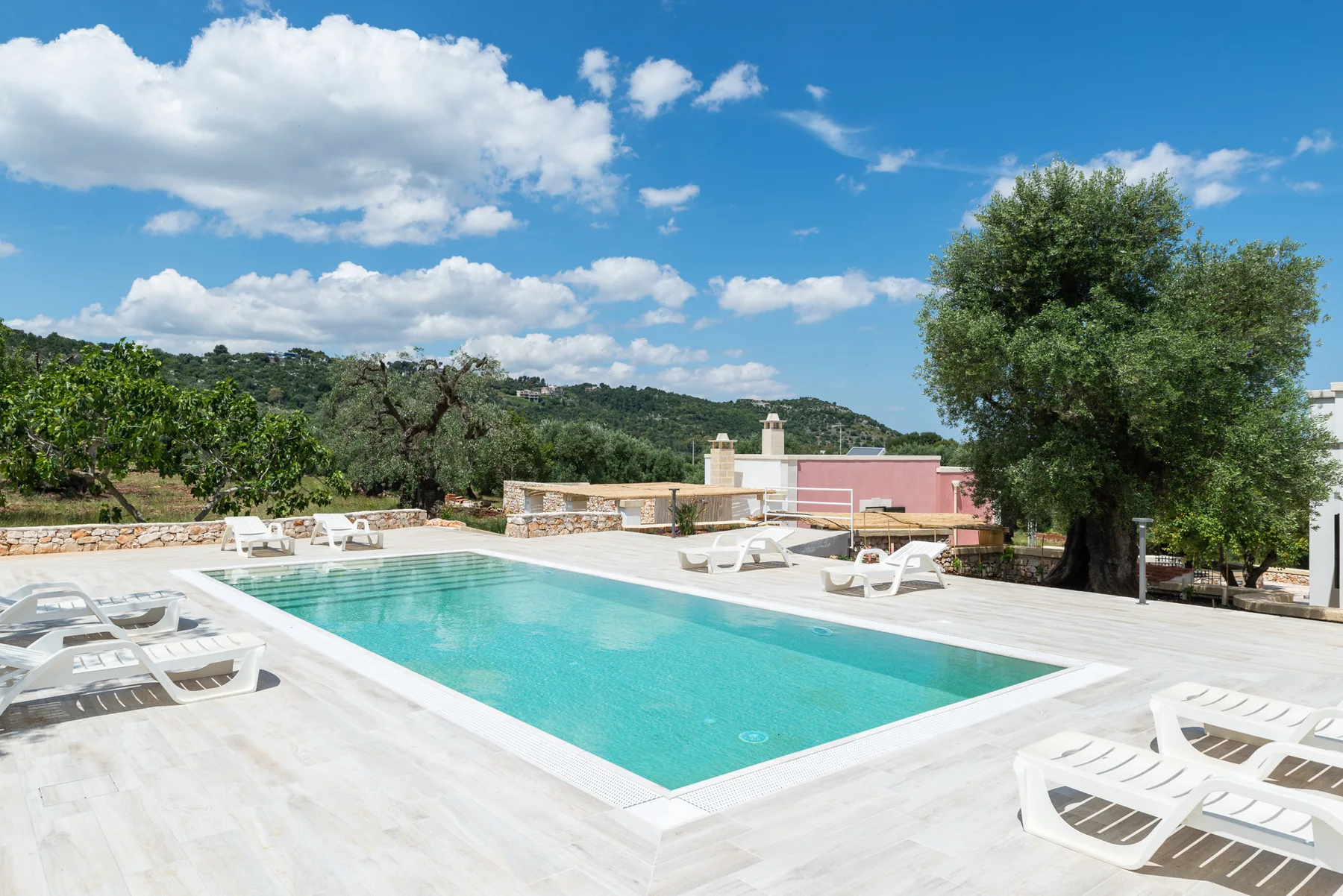 An outdoor swimming pool is surrounded by a pale stone deck and lounge chairs.