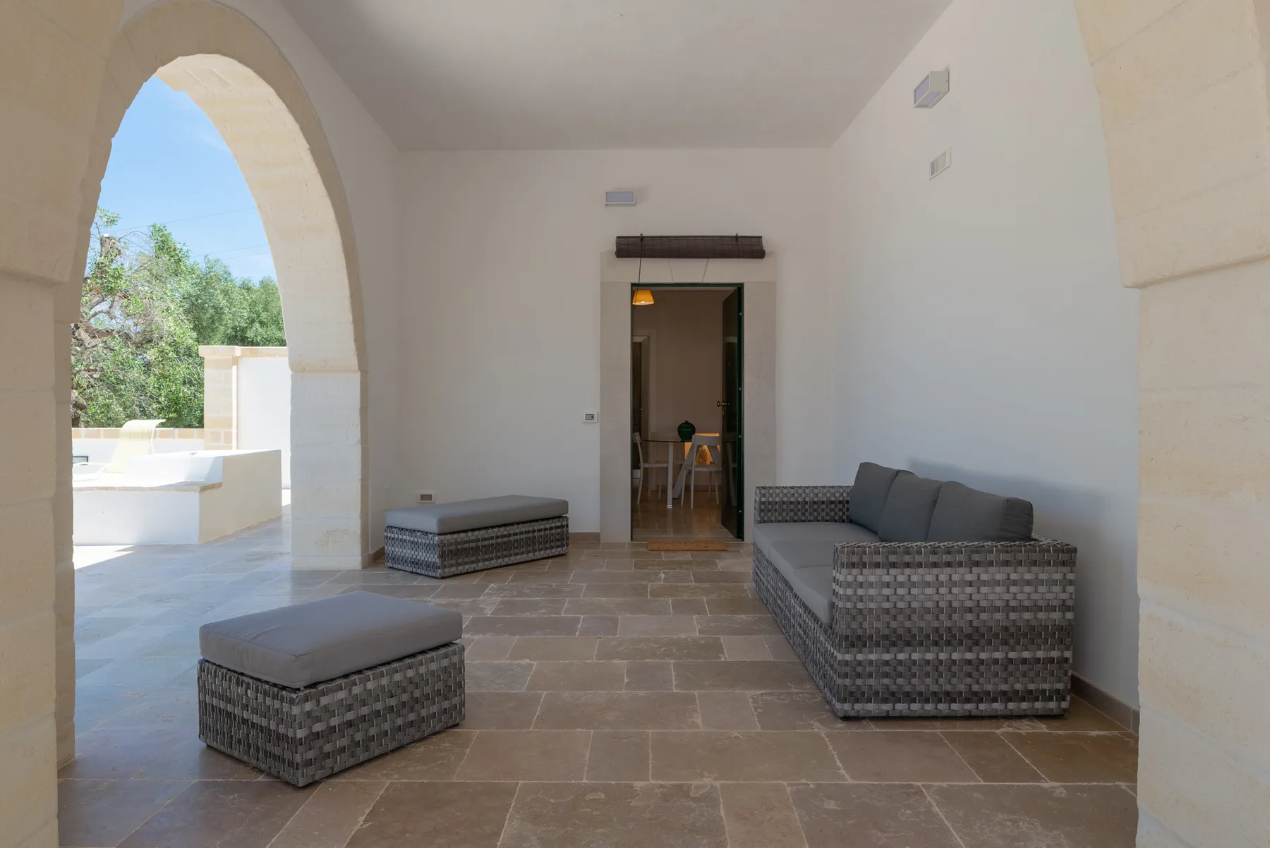A covered patio seating area with a view through an archway to greenery.