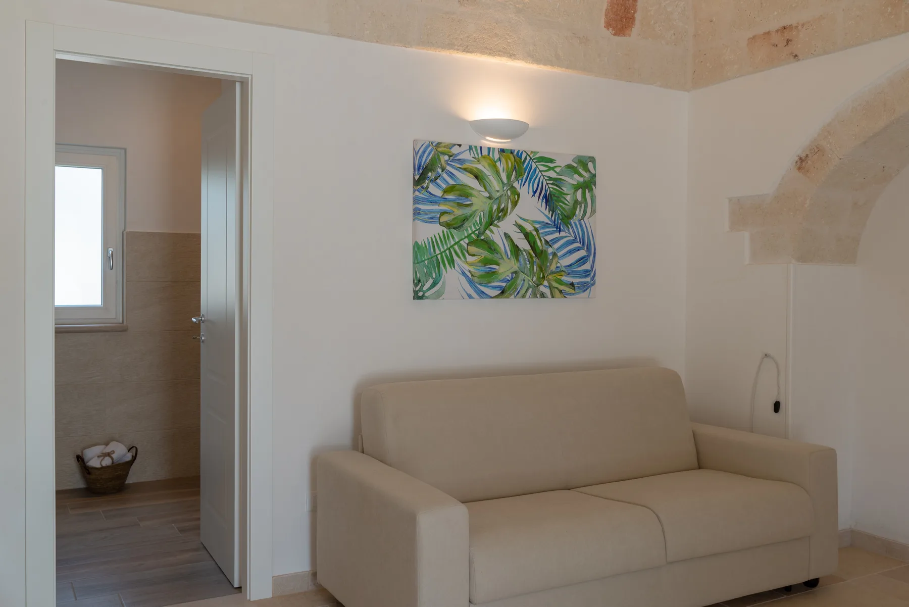 A small sitting area with a beige sofa beneath a colorful botanical painting.