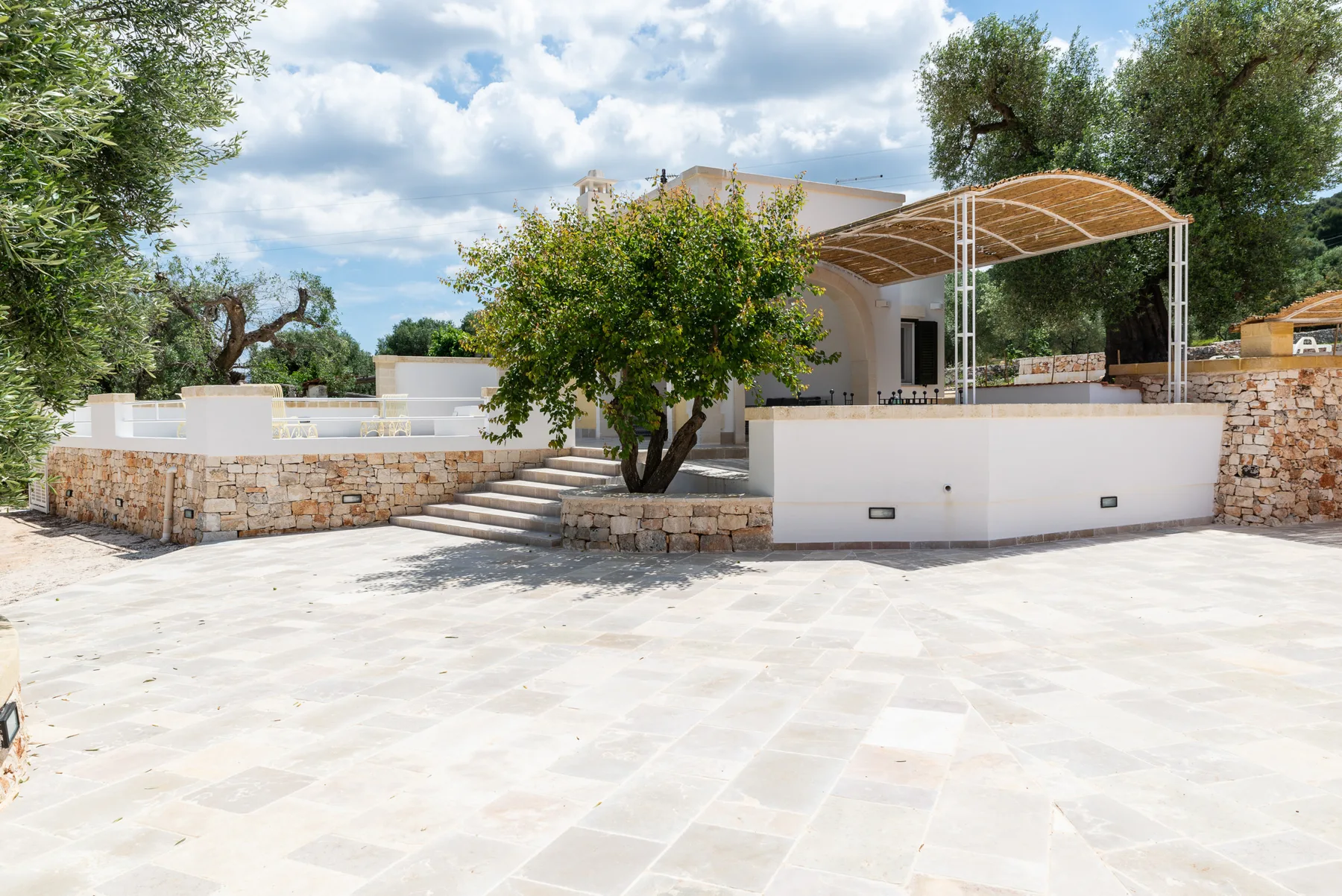 An outdoor patio with a stone wall, a tree, and a covered seating area.