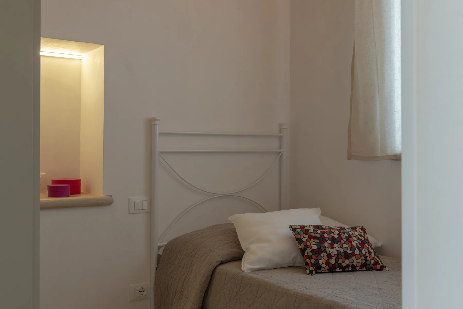 A bedroom with a bed, pillows, and a patterned cushion.