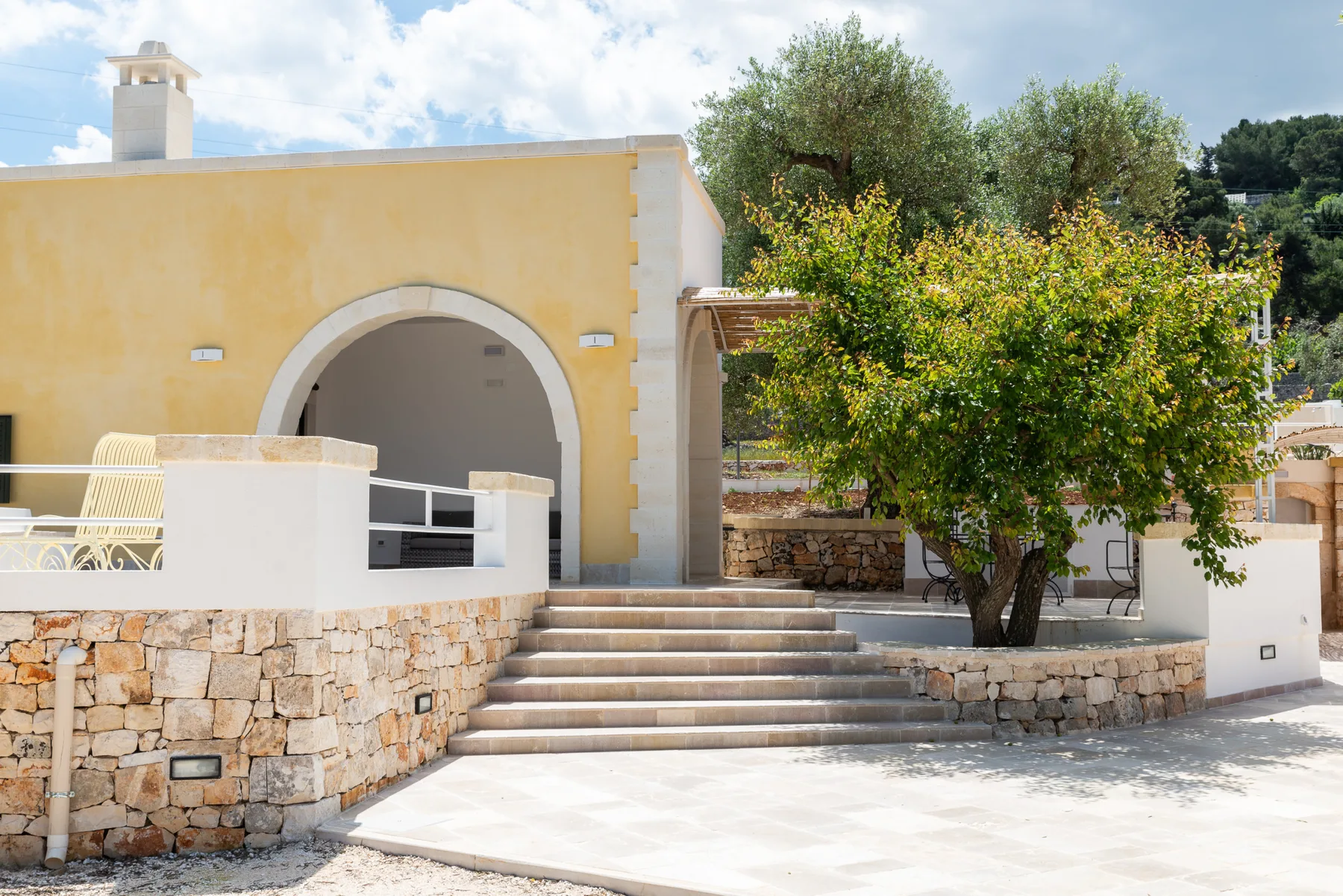A yellow exterior building with an arched entrance, stone steps, and trees.
