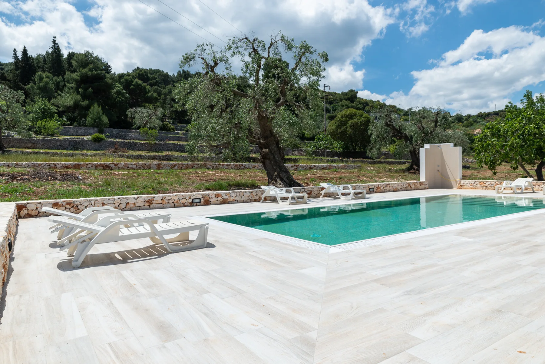 An outdoor swimming pool bordered by a pale deck and lounge chairs.