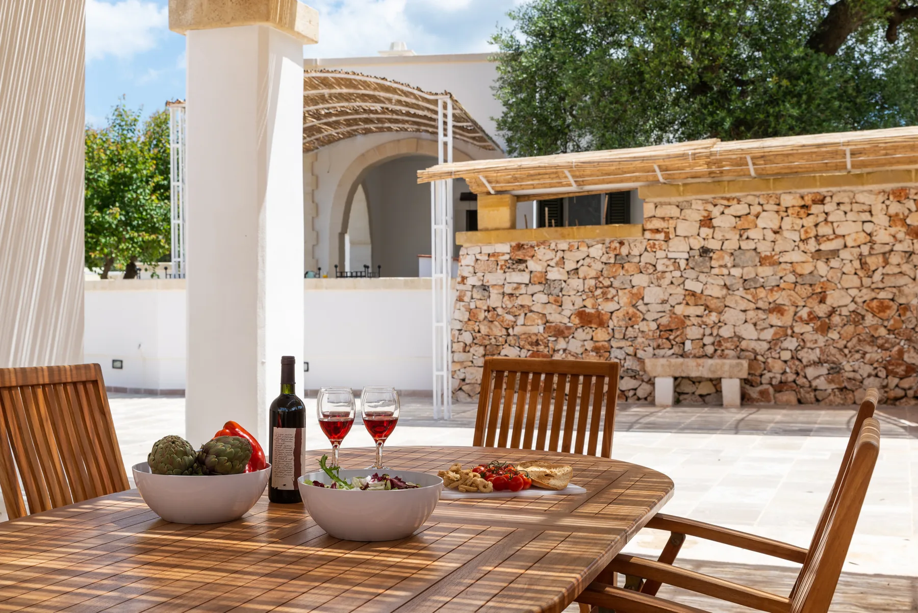 An outdoor dining area with a wooden table set beside a stone wall.