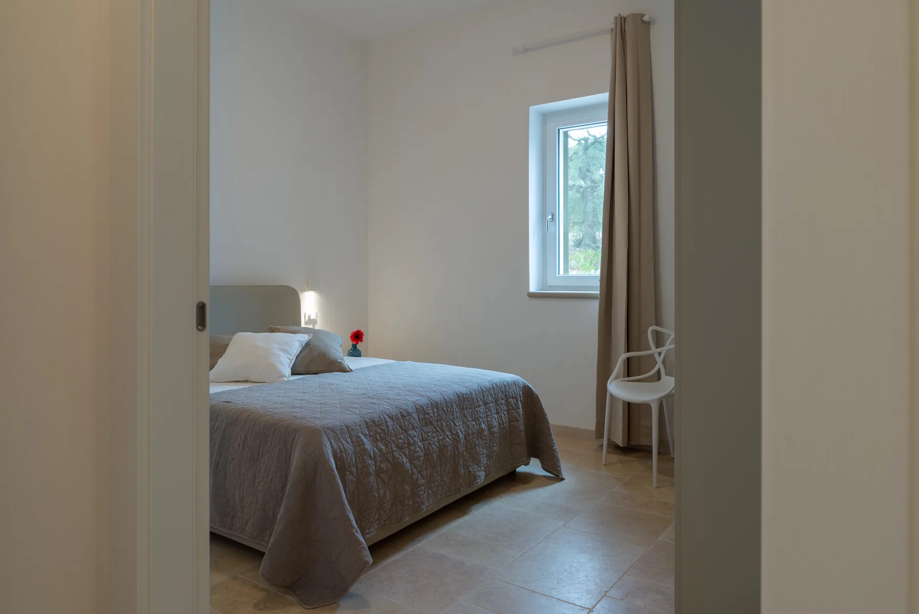 A bedroom with a neatly made bed, a window, and a chair.