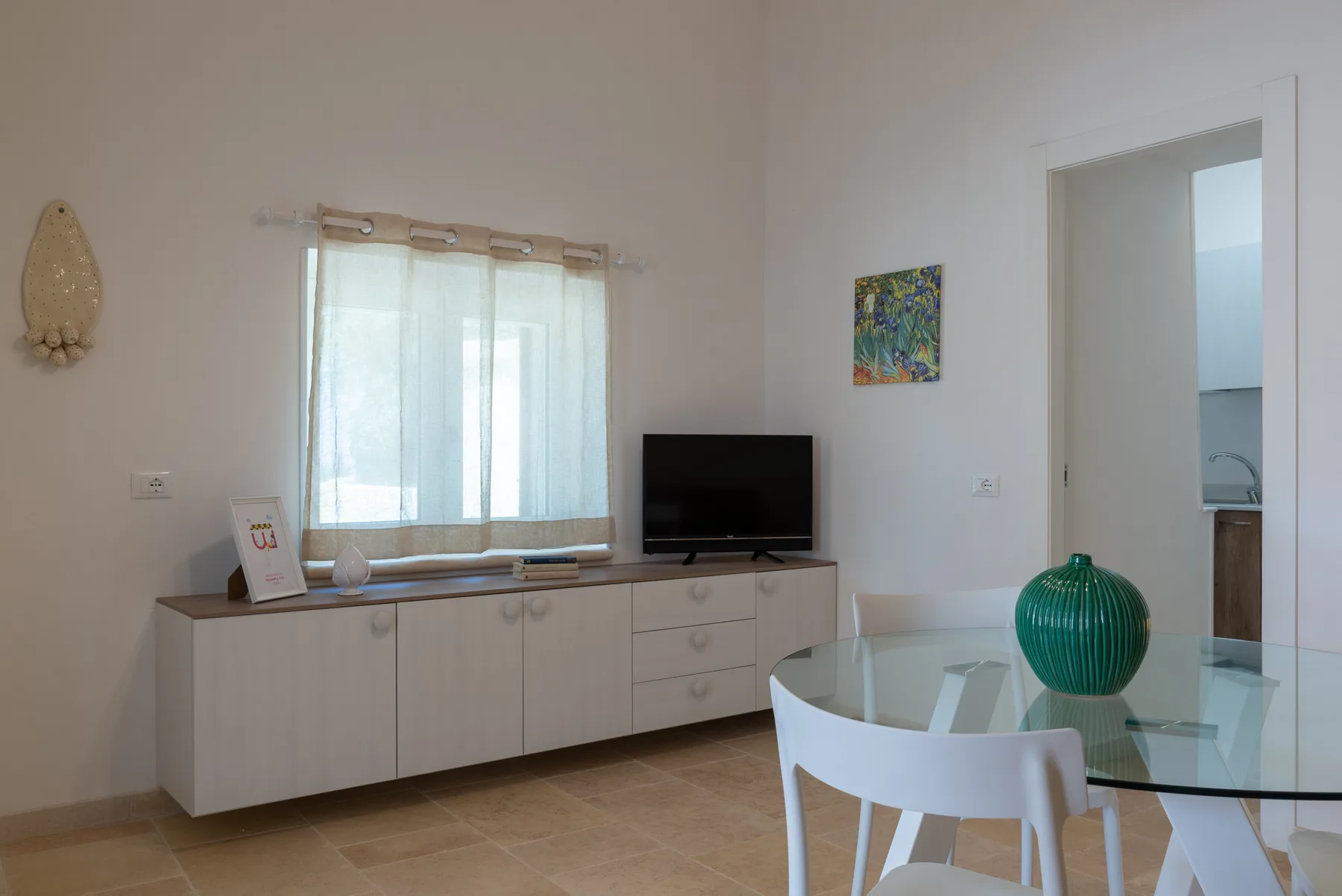 A bright living room with a television on a low cabinet and a glass dining table.