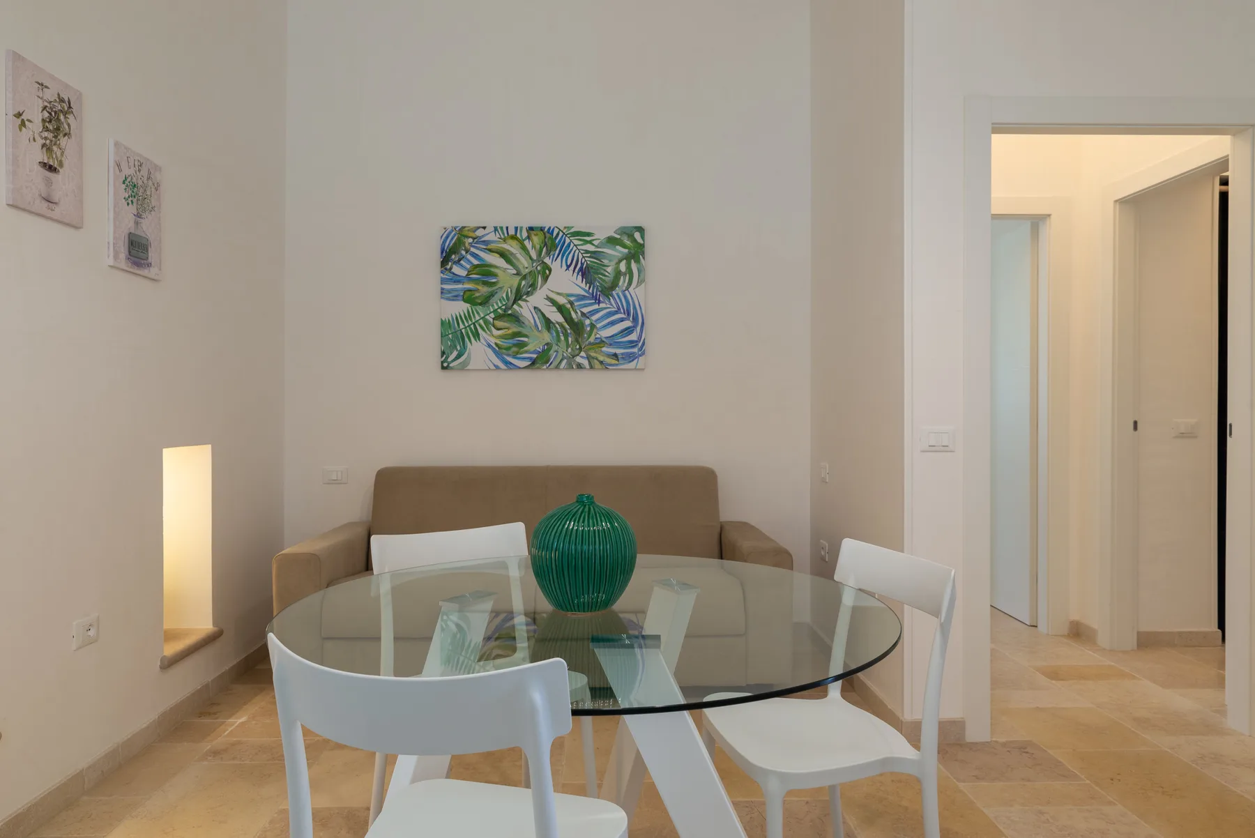 A dining area with a glass table and seating in front of a sofa.