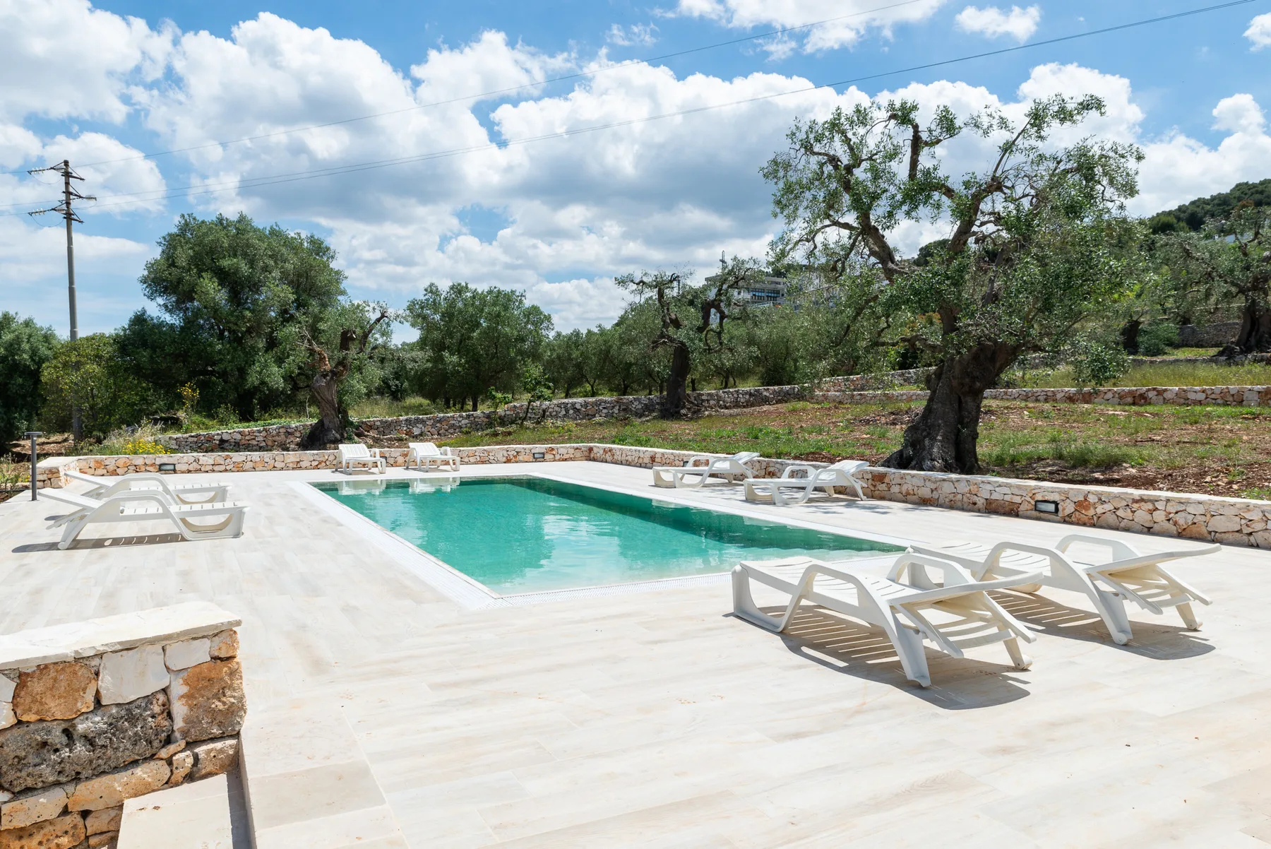 An outdoor swimming pool is surrounded by a pale stone deck and lounge seating.