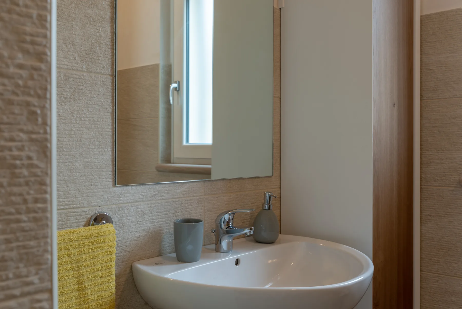 A bathroom sink sits beneath a large mirror beside a window.
