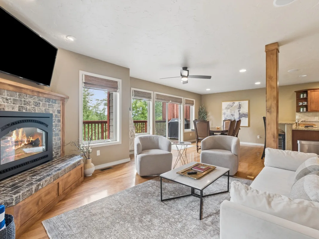 Unwind in your spacious living room featuring a cozy stone fireplace, plush seating, and expansive windows framing lush outdoor views—your perfect mountain retreat awaits.