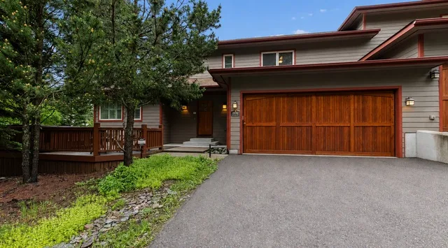 A modern house exterior with a wooden garage door, driveway, and surrounding trees.