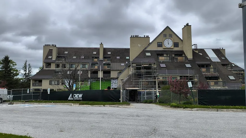 A large multi-story building with a steep roof and a clock faces a paved parking area.
