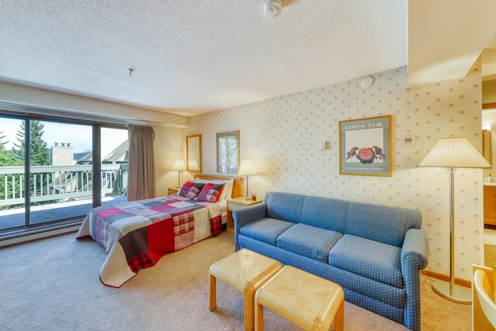A bedroom and sitting area with a bed, blue sofa, and balcony doors.