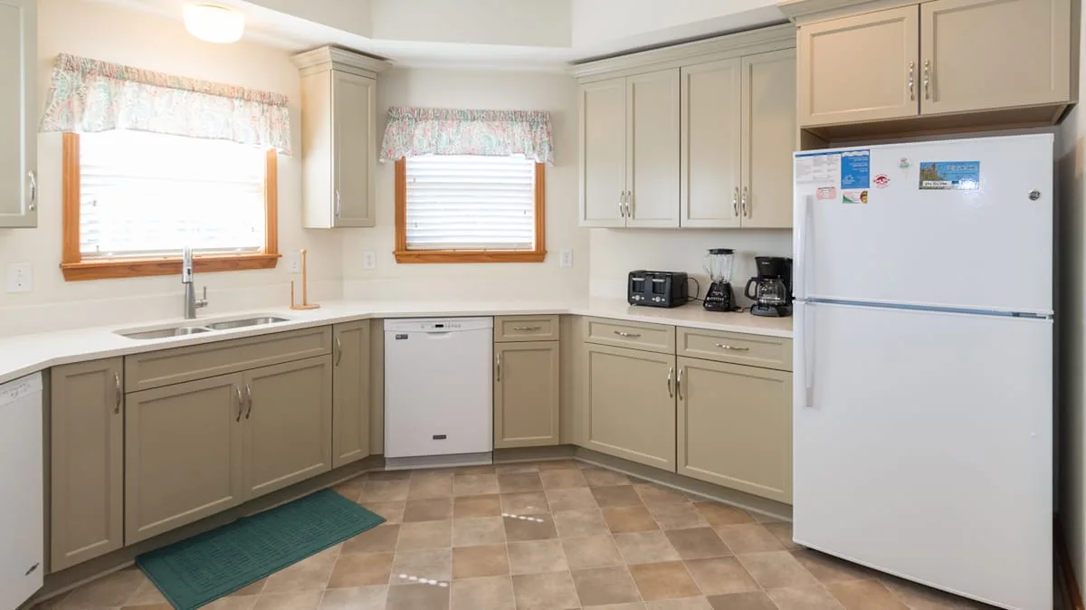 A bright kitchen with beige cabinets, a refrigerator, and windows above the counter.