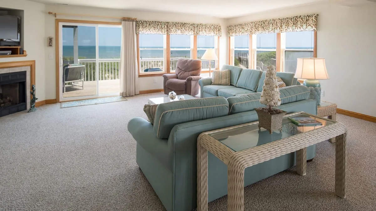 A bright living room with teal seating facing large windows and a coastal view.