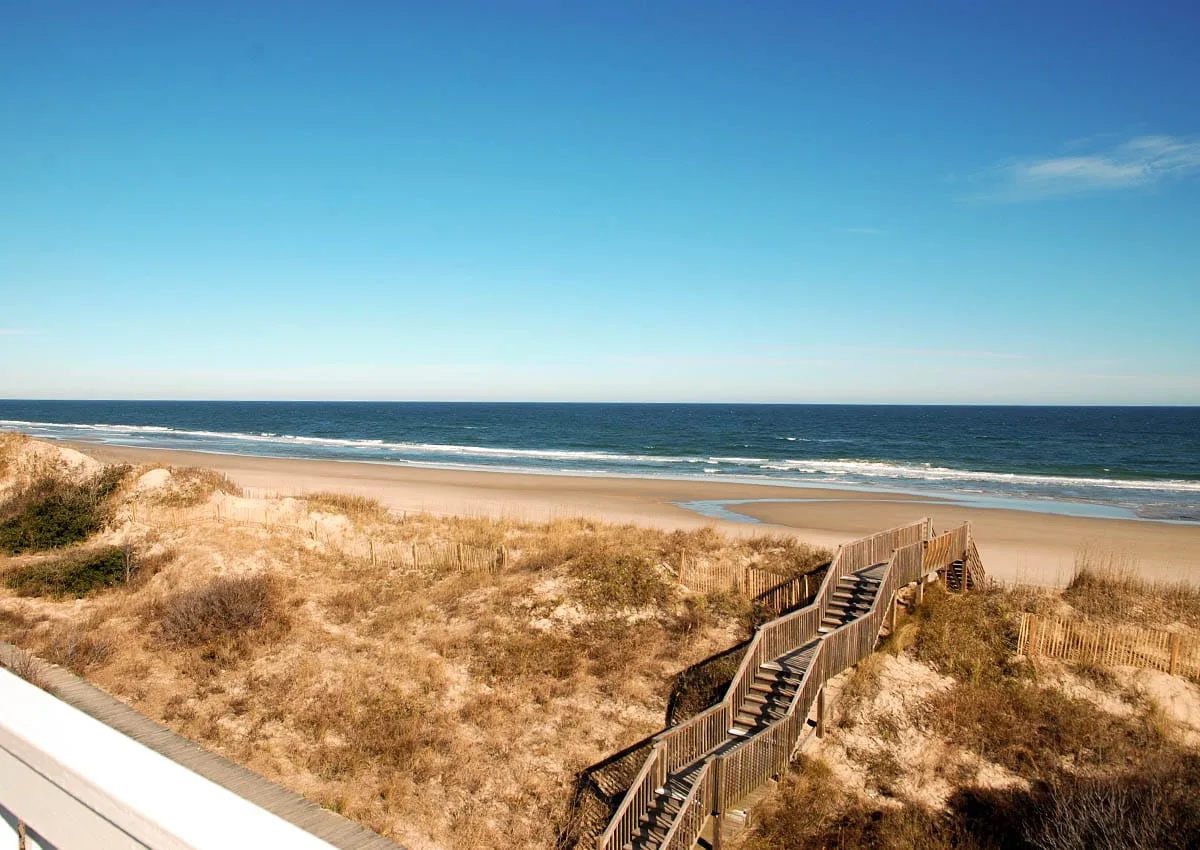 A wooden walkway crosses sandy dunes toward the beach and ocean.