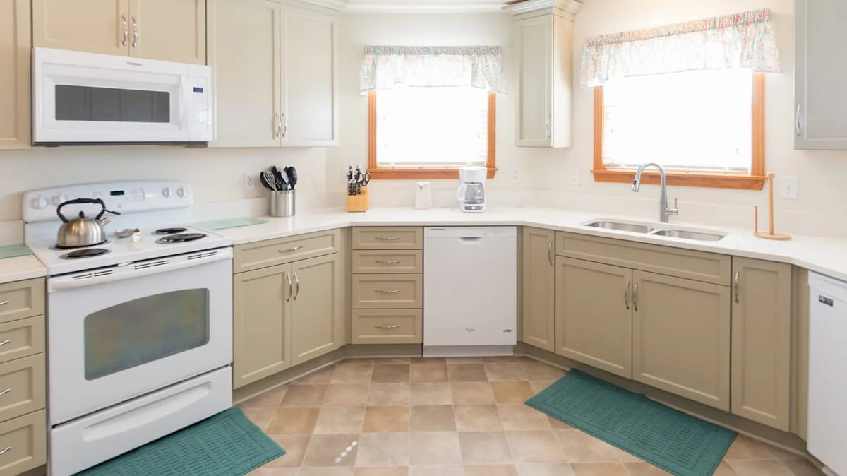 A bright kitchen with beige cabinets, a stove, and a sink.