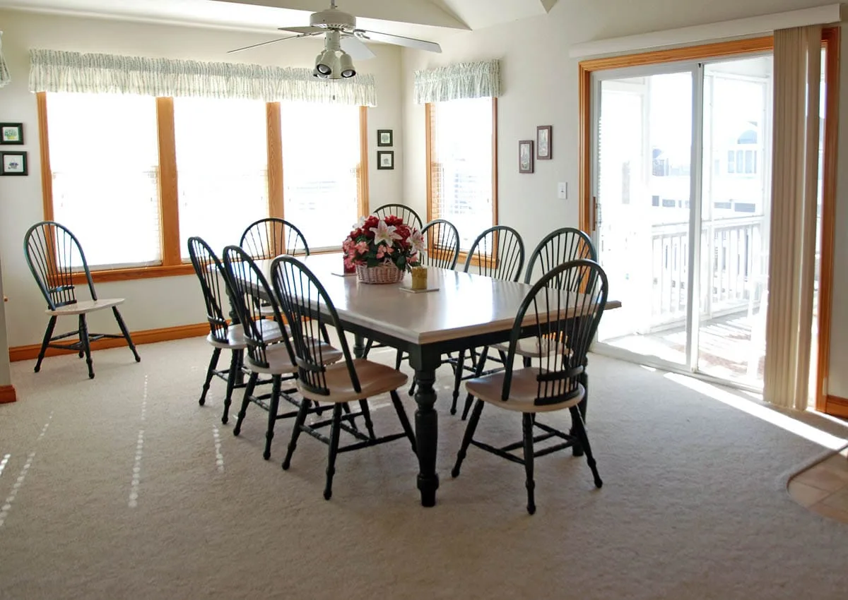 A dining room with a table and chairs beside large windows and a sliding glass door.