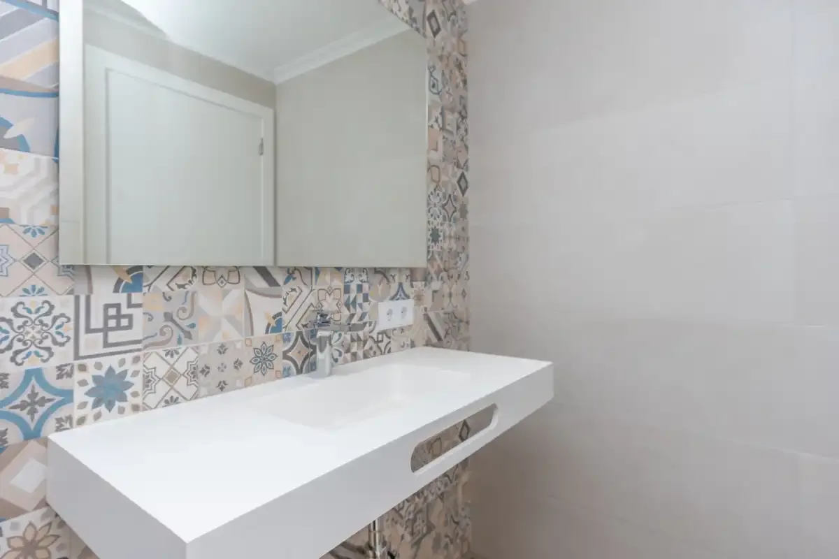 A bathroom vanity with a white countertop and patterned tile backsplash.