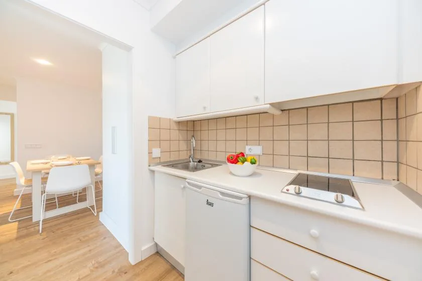A bright kitchen with white cabinets, a tiled backsplash, and a dining area beyond.