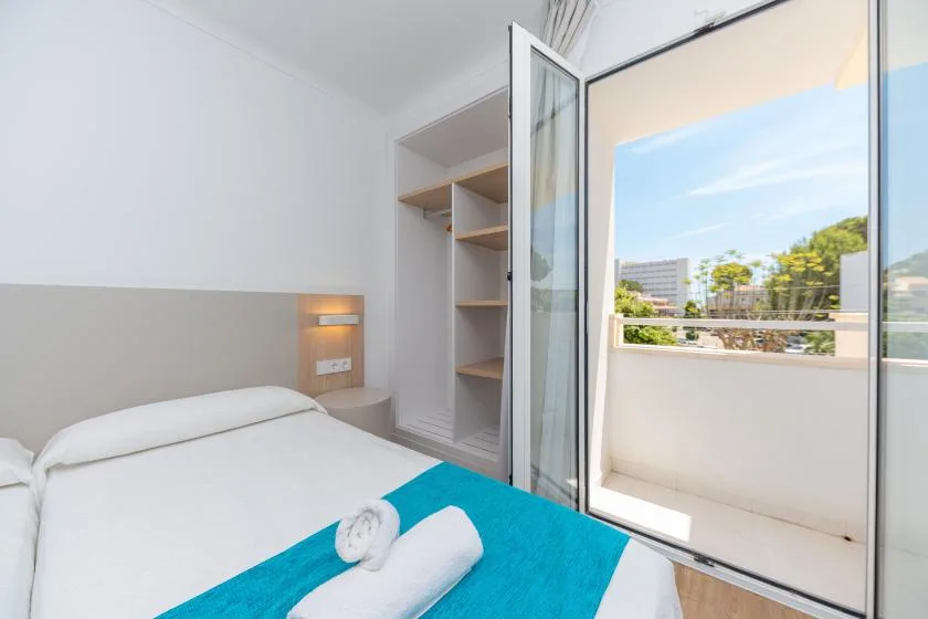 A bright bedroom with a bed beside an open balcony door.