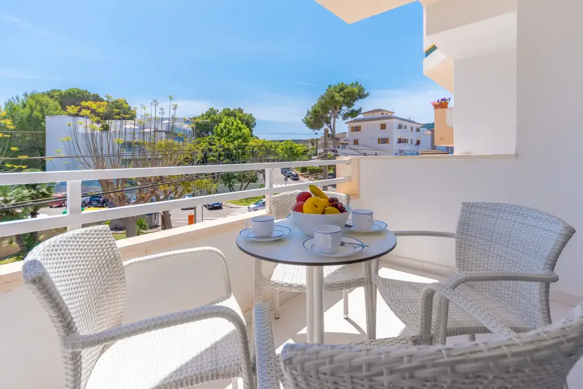 A balcony seating area with a round table overlooks nearby buildings and greenery.