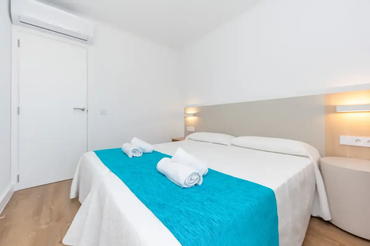 A bright bedroom with a double bed dressed in white and turquoise linens.