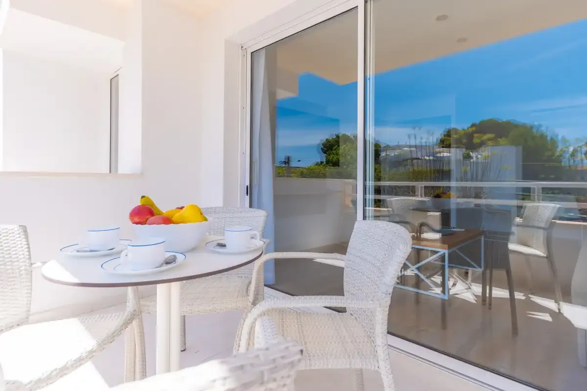 A bright patio dining area with white seating and a table set with cups and fruit.