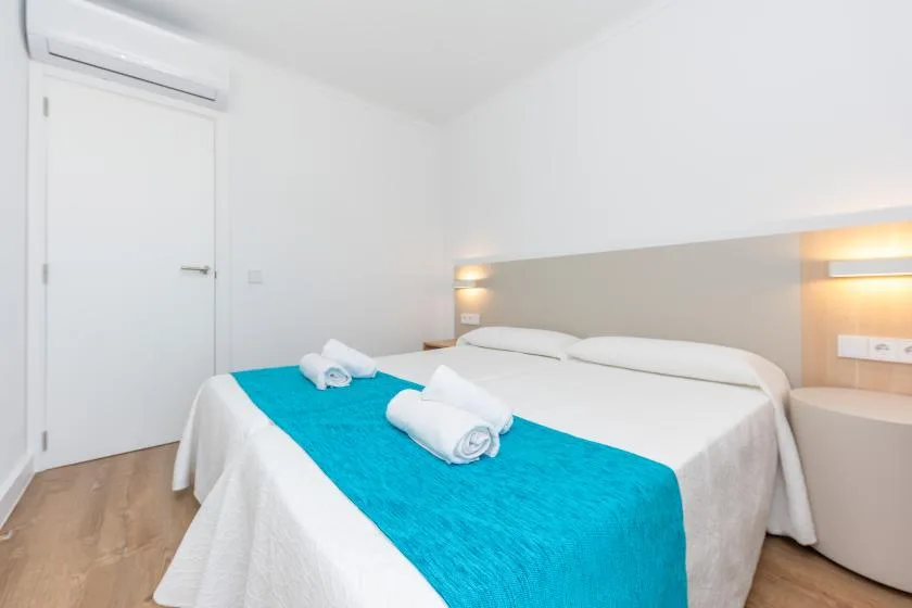 A bedroom with white bedding, a turquoise bed runner, and wall-mounted lights.