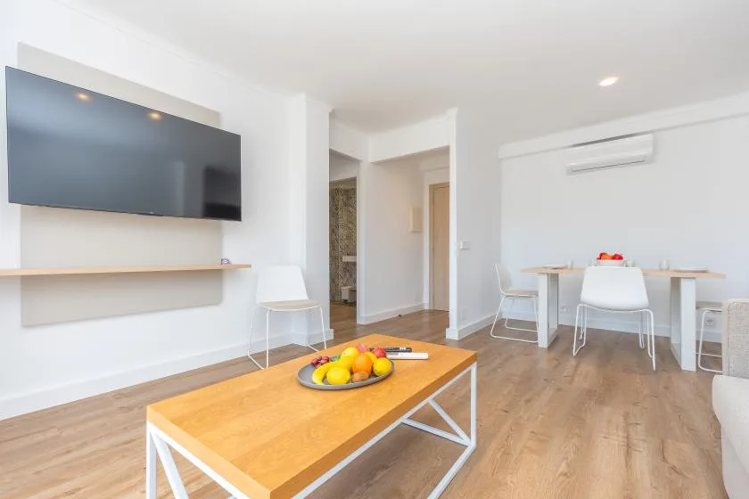 A bright living and dining area with a wall-mounted television and wooden table.