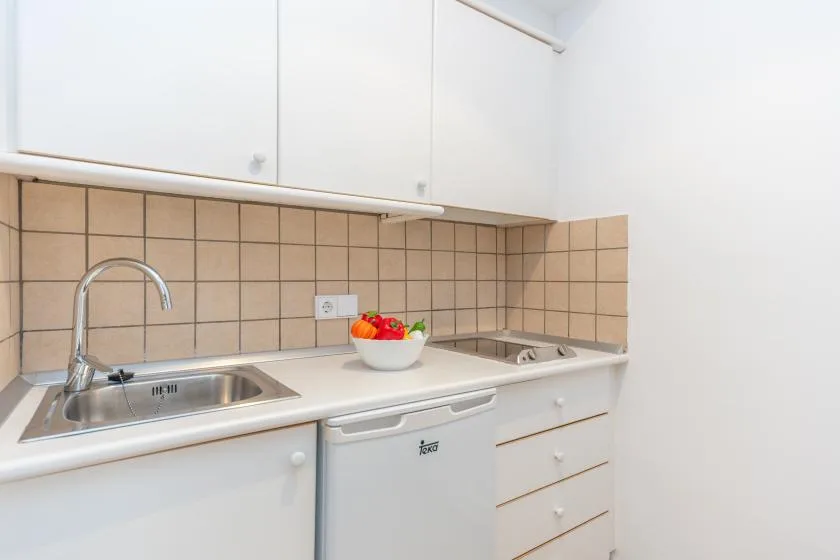 A compact kitchen counter with a sink, tiled backsplash, and white cabinets.