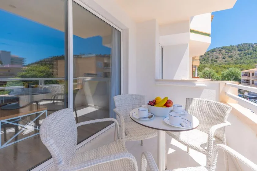 A sunny balcony with a round table, seating, and a fruit bowl.