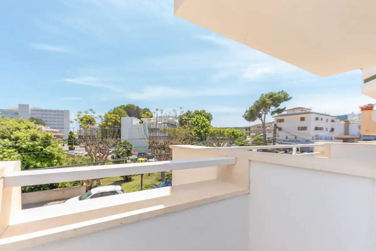 A balcony overlooks nearby buildings and trees beneath a blue sky.