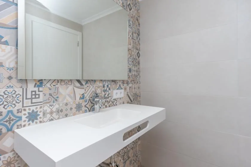 A bathroom vanity with a white basin against patterned and plain wall tiles.
