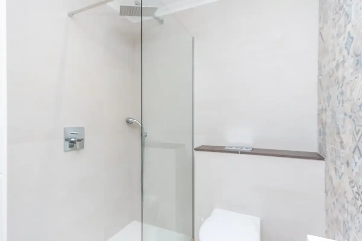 A bright bathroom with a glass shower and pale walls.